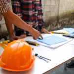 Workers at a table with drawings and one pointing out a detail