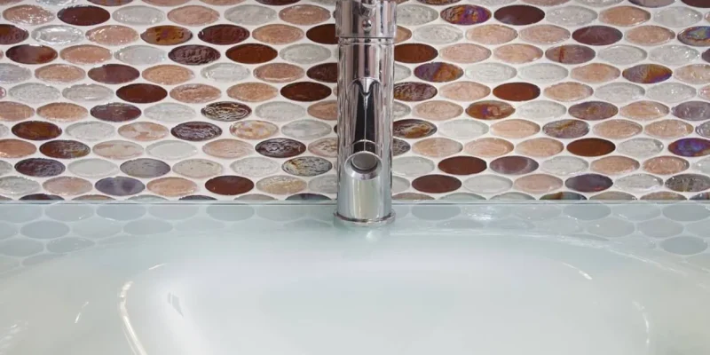 Close up of one piece sink with modern tap and 6" high tiled back splash with colored 3D glass oval insets that really pop